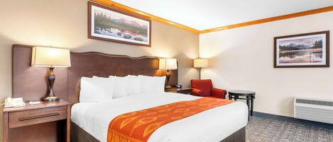 Un cuarto de hotel con una cama grande, dos lámparas de noche, una mesita de noche, una silla, una pequeña mesa y dos cuadros enmarcados en las paredes.