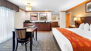 Una habitación de hotel con cama, escritorio, silla, kitchenette y baño.