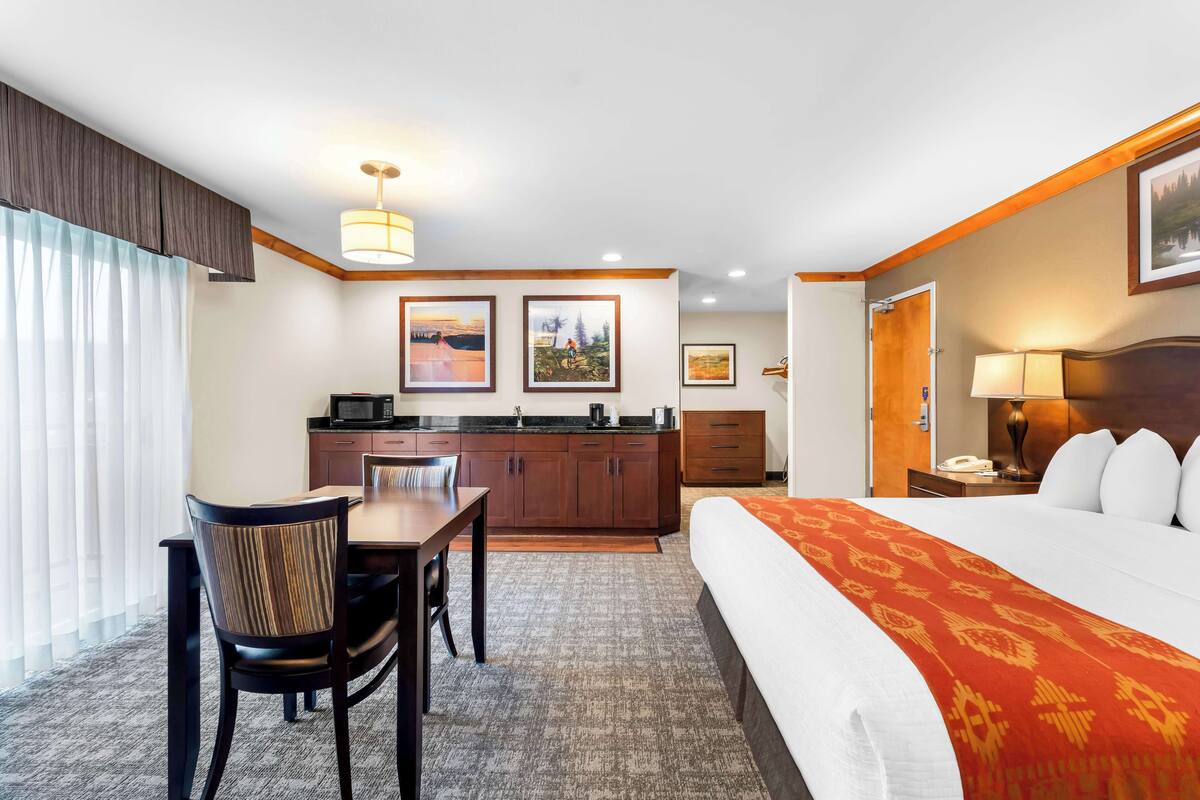Een hotelkamer met een bed, een bureau, een stoel, een kitchenette en een badkamer.