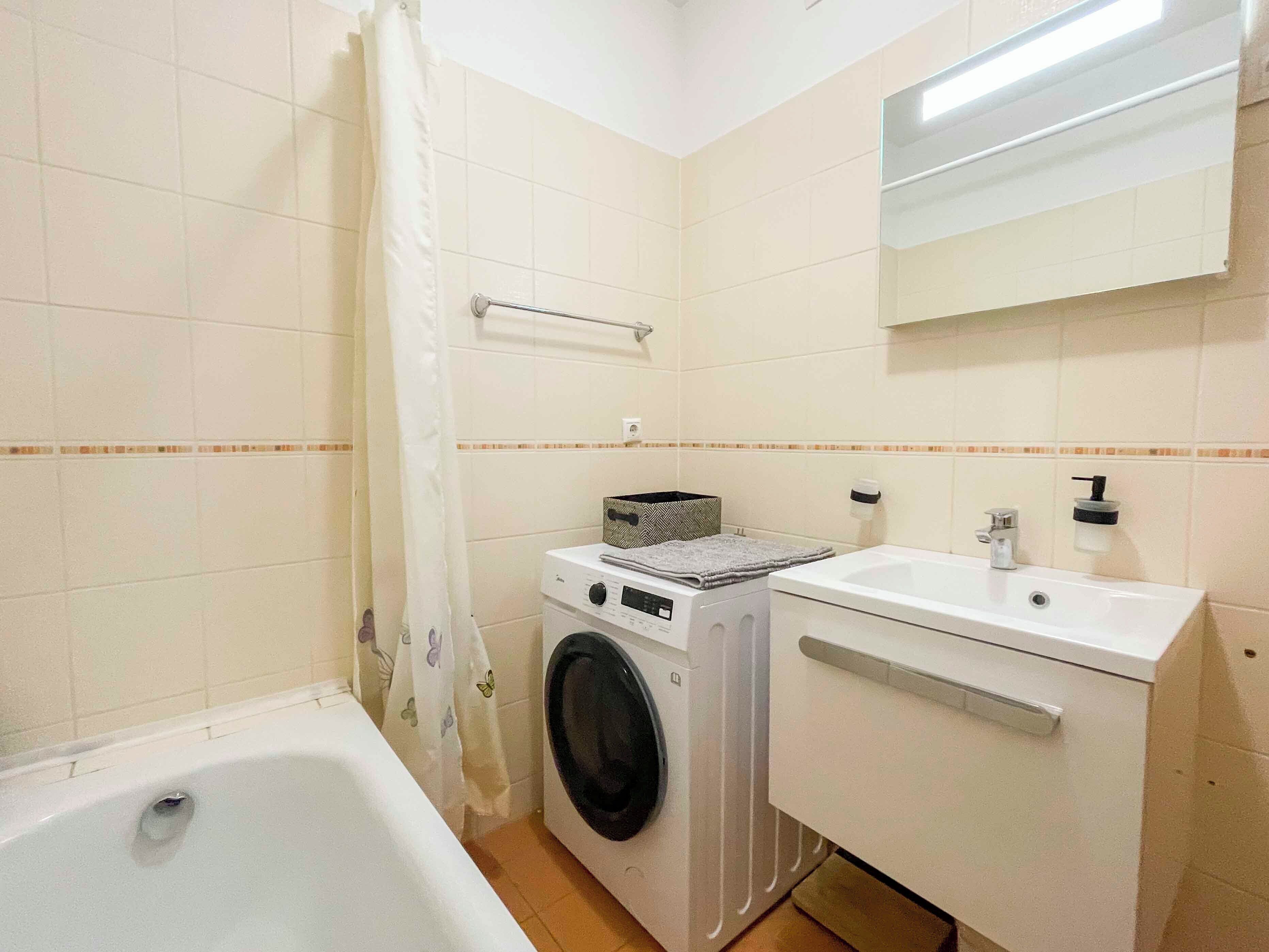 A compact bathroom with a bathtub, a washing machine, and a sink.
