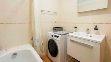 A compact bathroom with a bathtub, a washing machine, and a sink.
