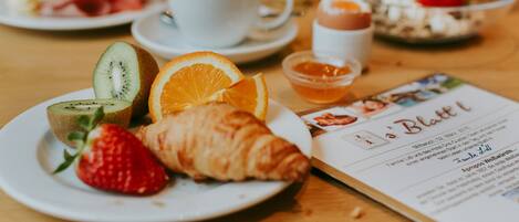 Desayuno con cruasanes, fresas, kiwi, rodajas de naranja y una taza de café sobre una mesa.