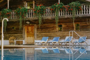 A wooden cabin with a pool, blue-striped lounge chairs, and hanging flower baskets. - Hotel Drei Quellen Therme (Bad Griesbach im Rottal)