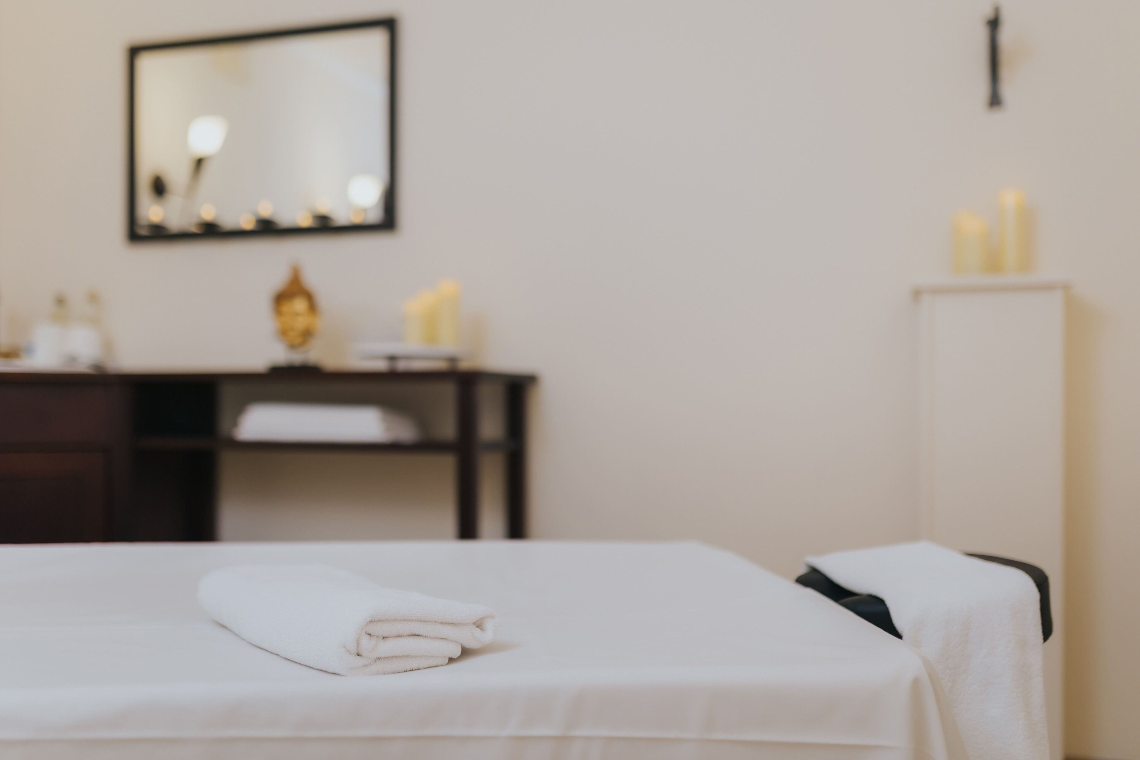 A neatly made bed with a folded white towel, a mirror on the wall, and a small table with toiletries.