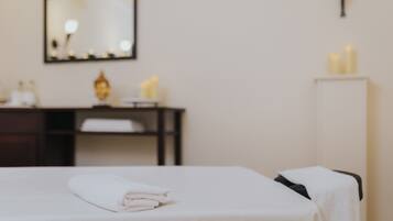 A neatly made bed with a folded white towel, a mirror on the wall, and a small table with toiletries.