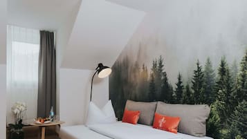 A modern hotel room with a bed, a nightstand, a lamp, and a mural of a forest.