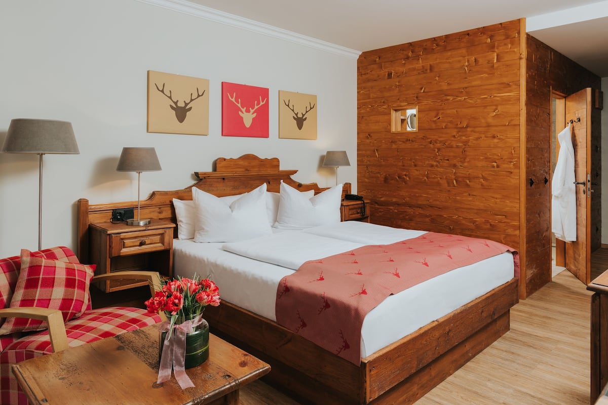 A wooden-framed bedroom with a bed, two bedside tables, a nightstand, a chair, and a table with a vase of flowers.