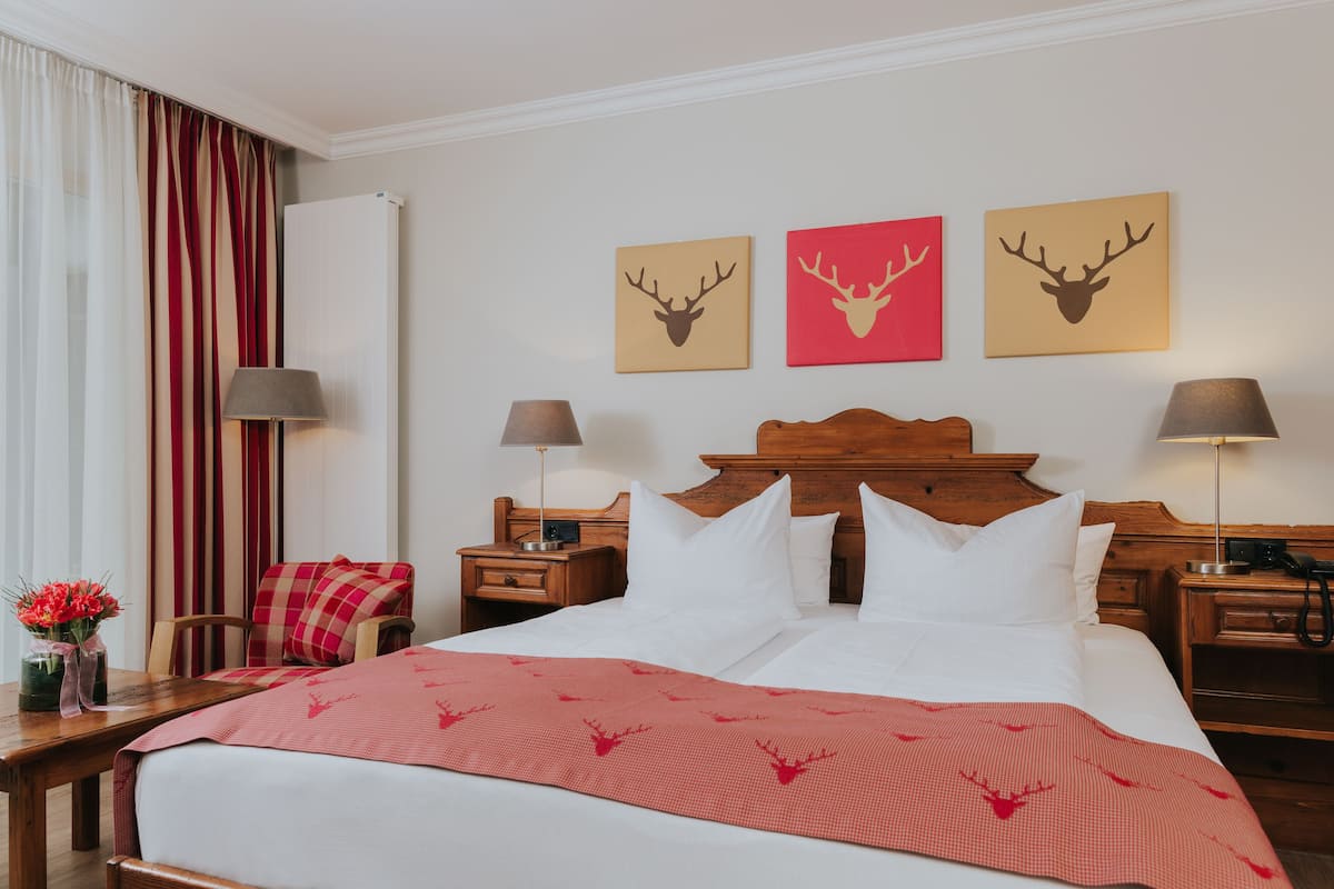 A hotel room with a large bed, two bedside tables, a wooden headboard, a red and white striped curtain, and three wall-mounted deer head paintings.