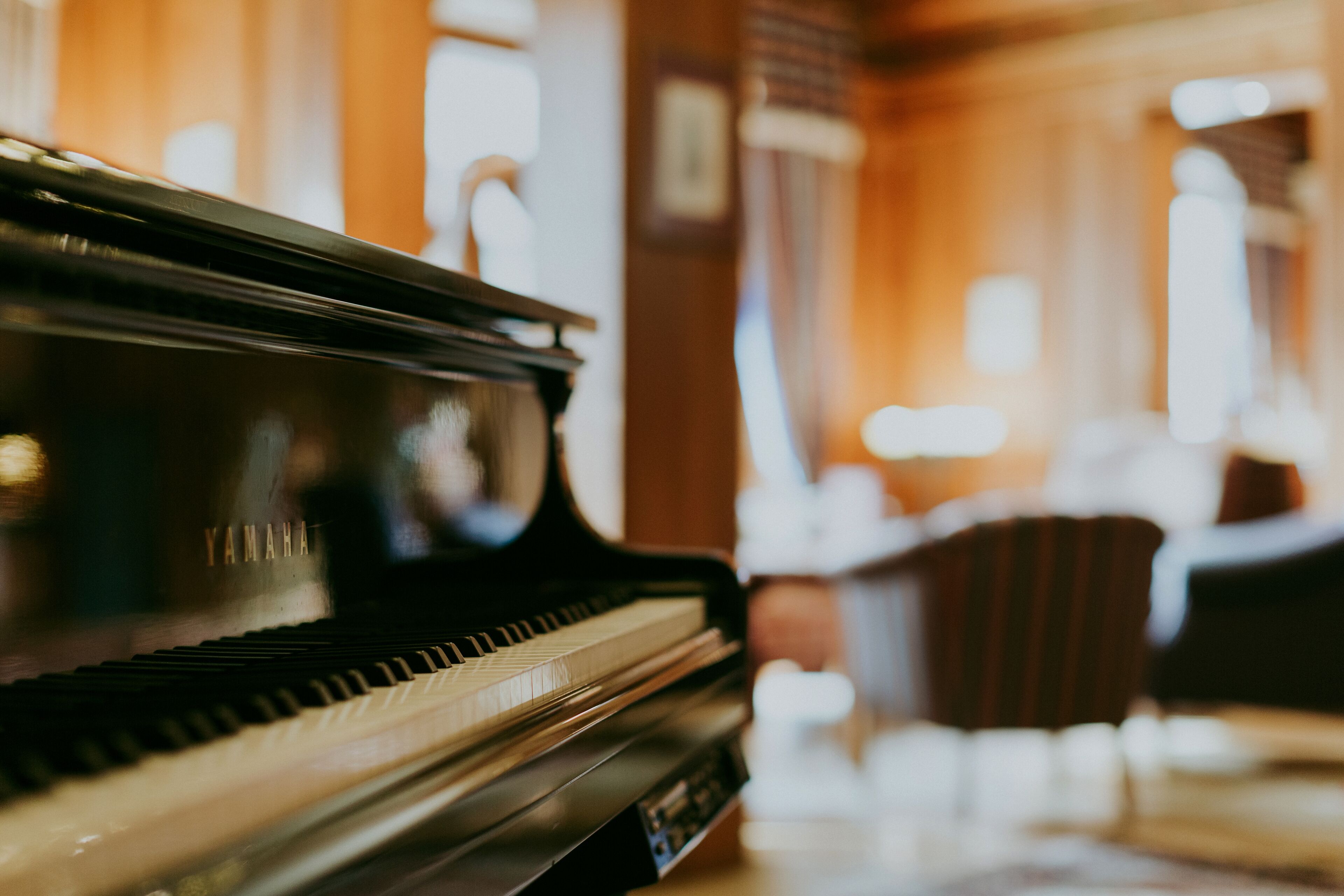 A grand piano in a warmly lit room with wooden paneling and a chair in the background.