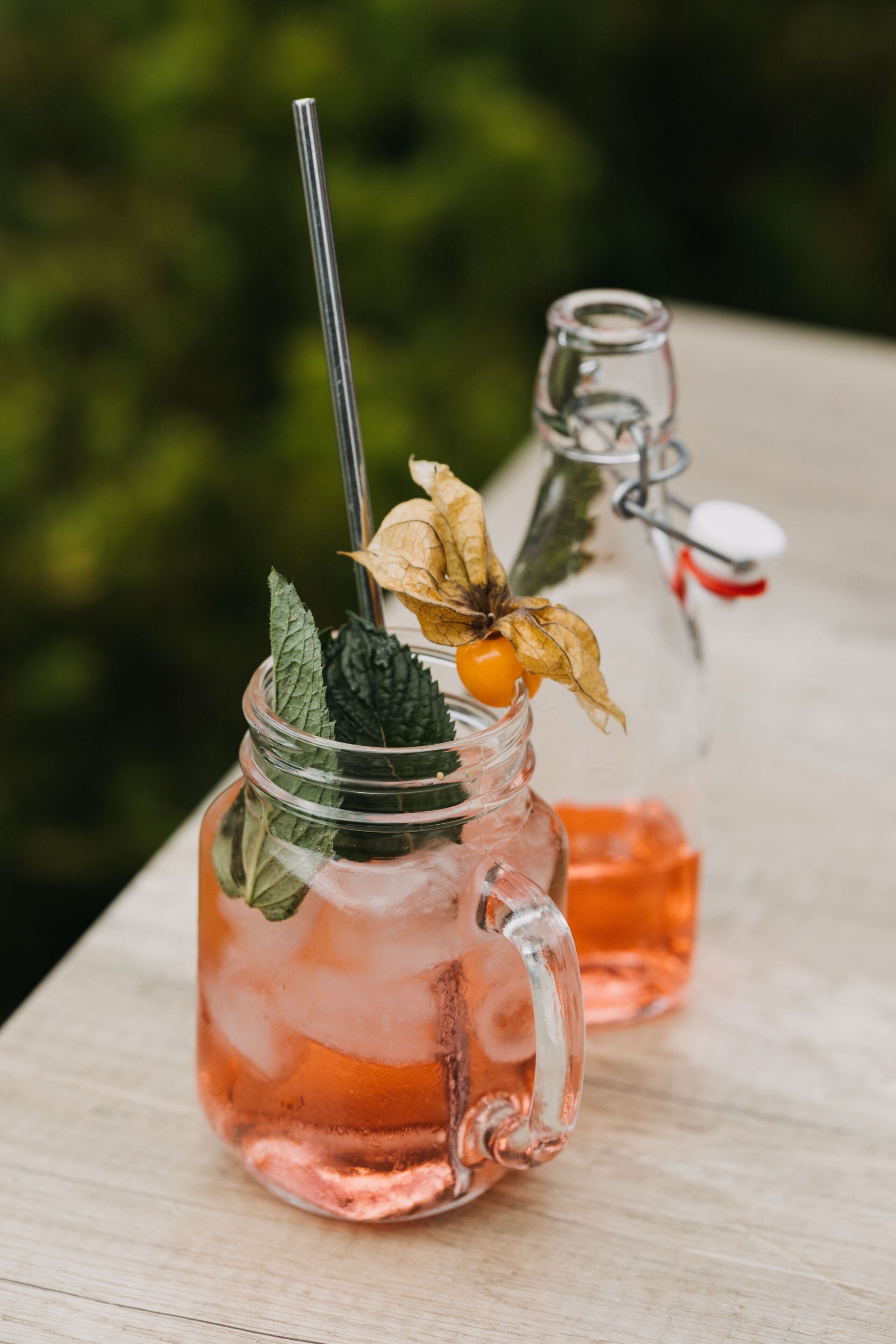 Two glass mugs with handles, filled with a pink liquid, possibly a beverage, and garnished with a flower and mint leaves.