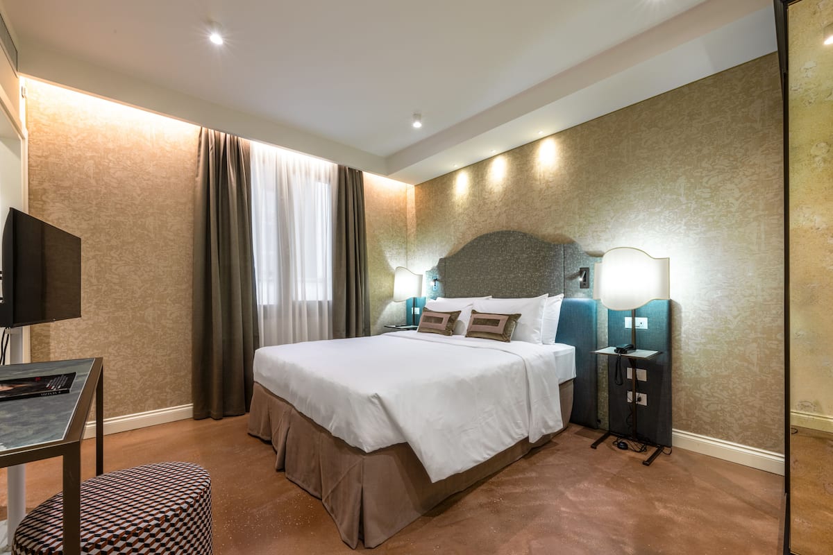 A hotel room with a large bed, a desk, a TV, and a lamp.