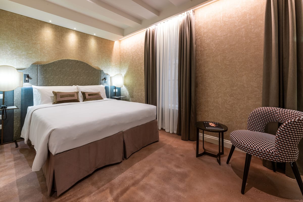 A hotel room with a large bed, a chair, a nightstand, and a lamp.