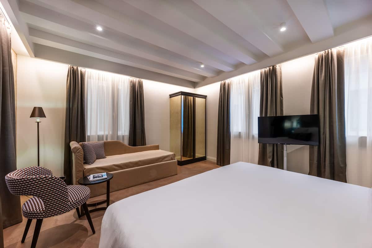 A hotel room with a bed, a sofa, a chair, a TV, and a mirror.