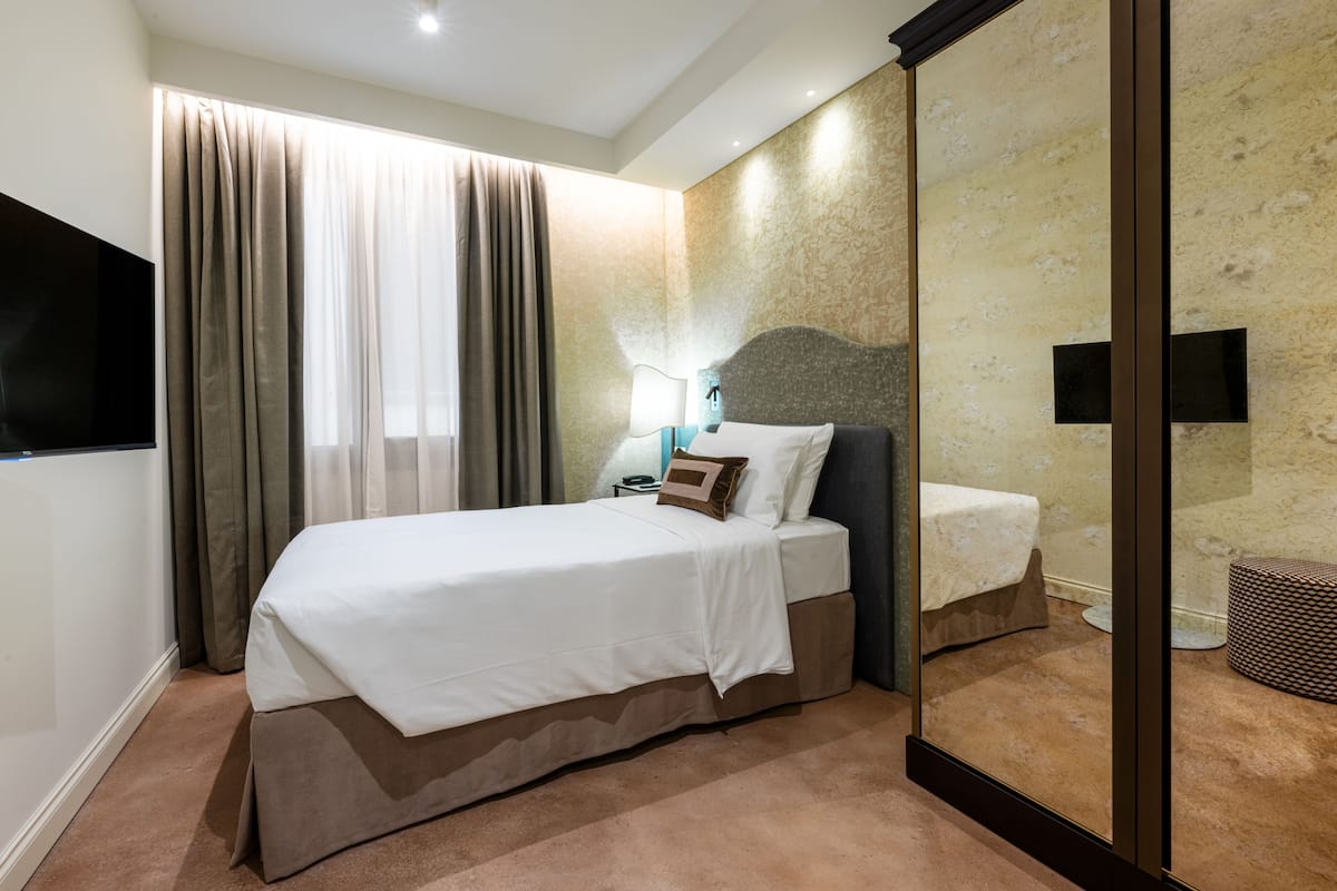 A hotel room with a bed, a TV, a nightstand, and a mirror.