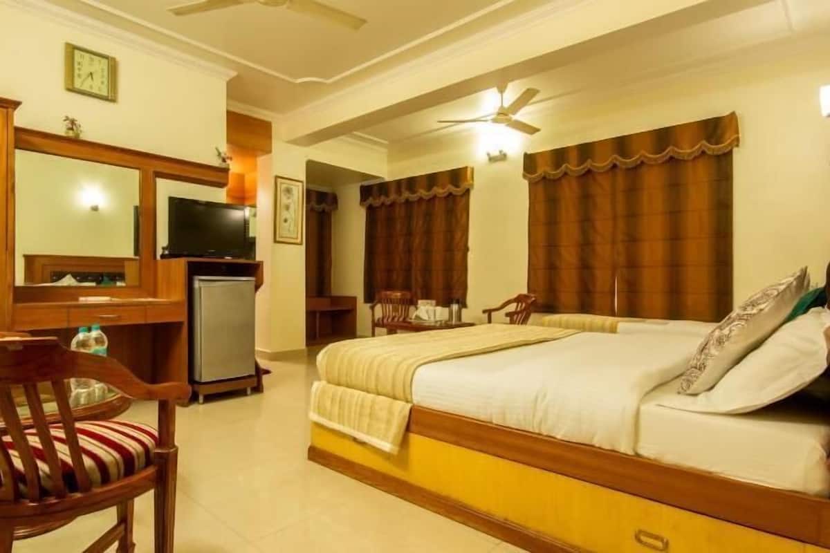 A hotel room with a bed, a desk with a television, a refrigerator, and a chair.