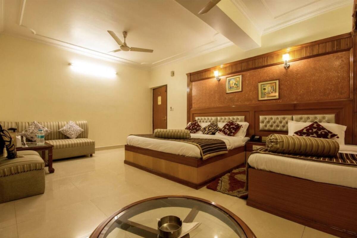 A hotel room with two beds, a sofa, a glass coffee table, and a ceiling fan.