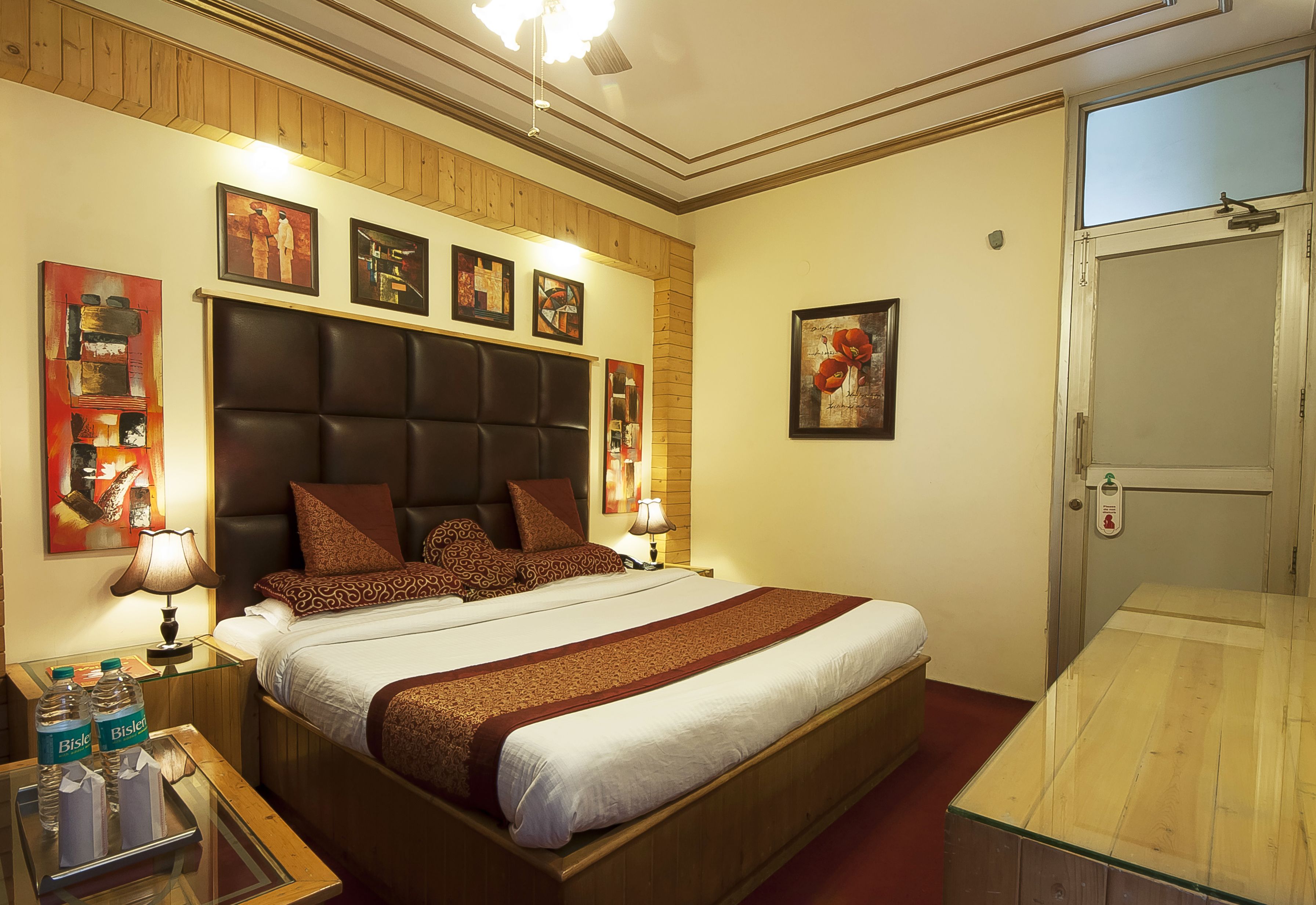 Habitación de hotel con una cama grande, cabecera de madera, varias almohadas, mesitas de noche con lámparas y obras de arte en las paredes.