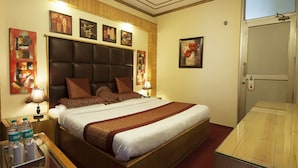 A hotel room with a large bed, wooden headboard, multiple pillows, bedside tables with lamps, and artwork on the walls. - Hotel lals Haveli (New Delhi)