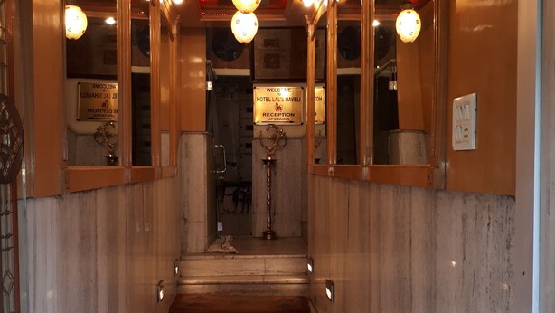 A hallway with marble walls, a polished floor, and a reception desk with a sign. - Hotel lals Haveli (New Delhi)