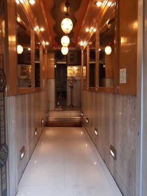 A hallway with marble walls, a polished floor, and a reception desk with a sign. - Hotel lals Haveli (New Delhi)