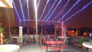 An outdoor patio area with tables and chairs, potted plants, and string lights. - Hotel lals Haveli (New Delhi)
