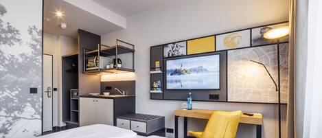 A modern hotel room with a bed, a desk with a chair, a TV, and a map on the wall.