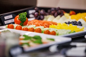 A buffet table with various fruits and vegetables, including tomatoes, cucumbers, and grapes.