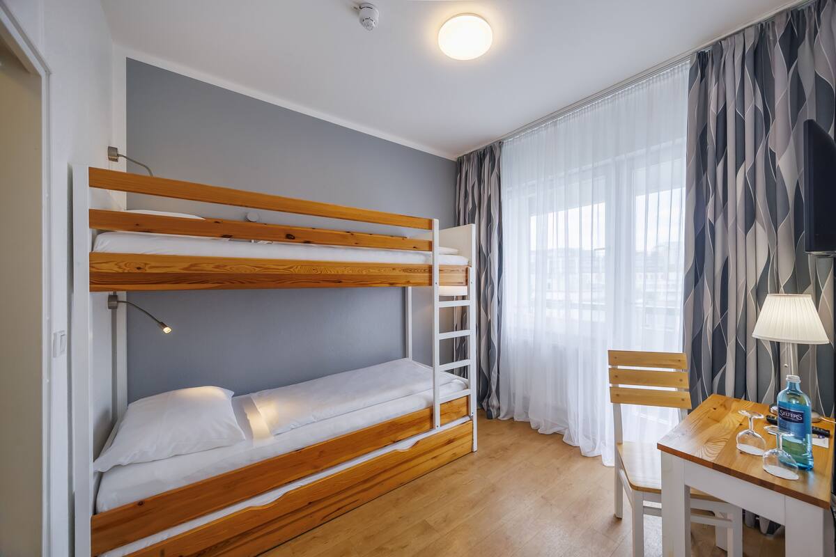 A bunk bed room with a desk, lamp, and curtains.
