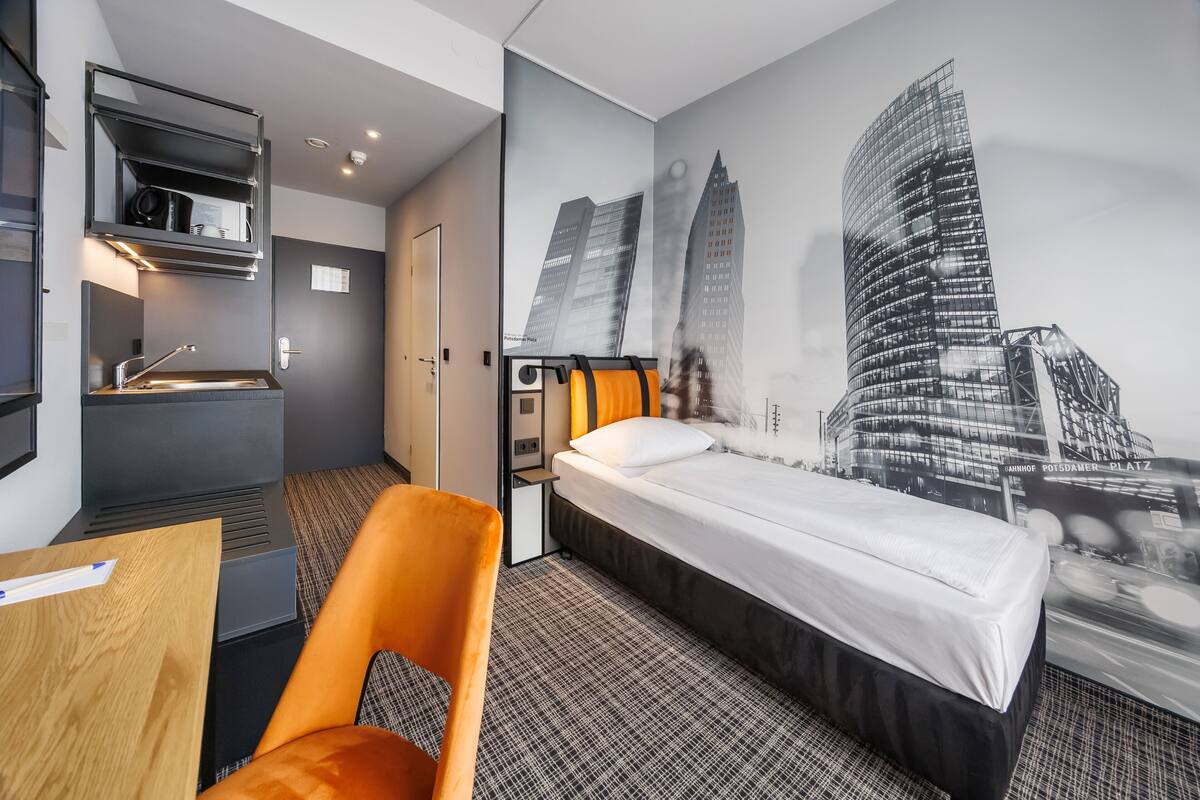 A hotel room with a bed, a desk, a chair, a bathroom, and a cityscape mural on the wall.