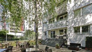 Ulkoterassi, jossa on pöytiä ja tuoleja, sekä portaikko, joka johtaa rakennukseen, jonka yläpuolella on kyltti, jossa lukee ”CAFE LÜTZOW”.