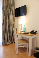 Un pequeño espacio de oficina con un escritorio, una silla, una lámpara, un teléfono y un televisor montado en la pared.