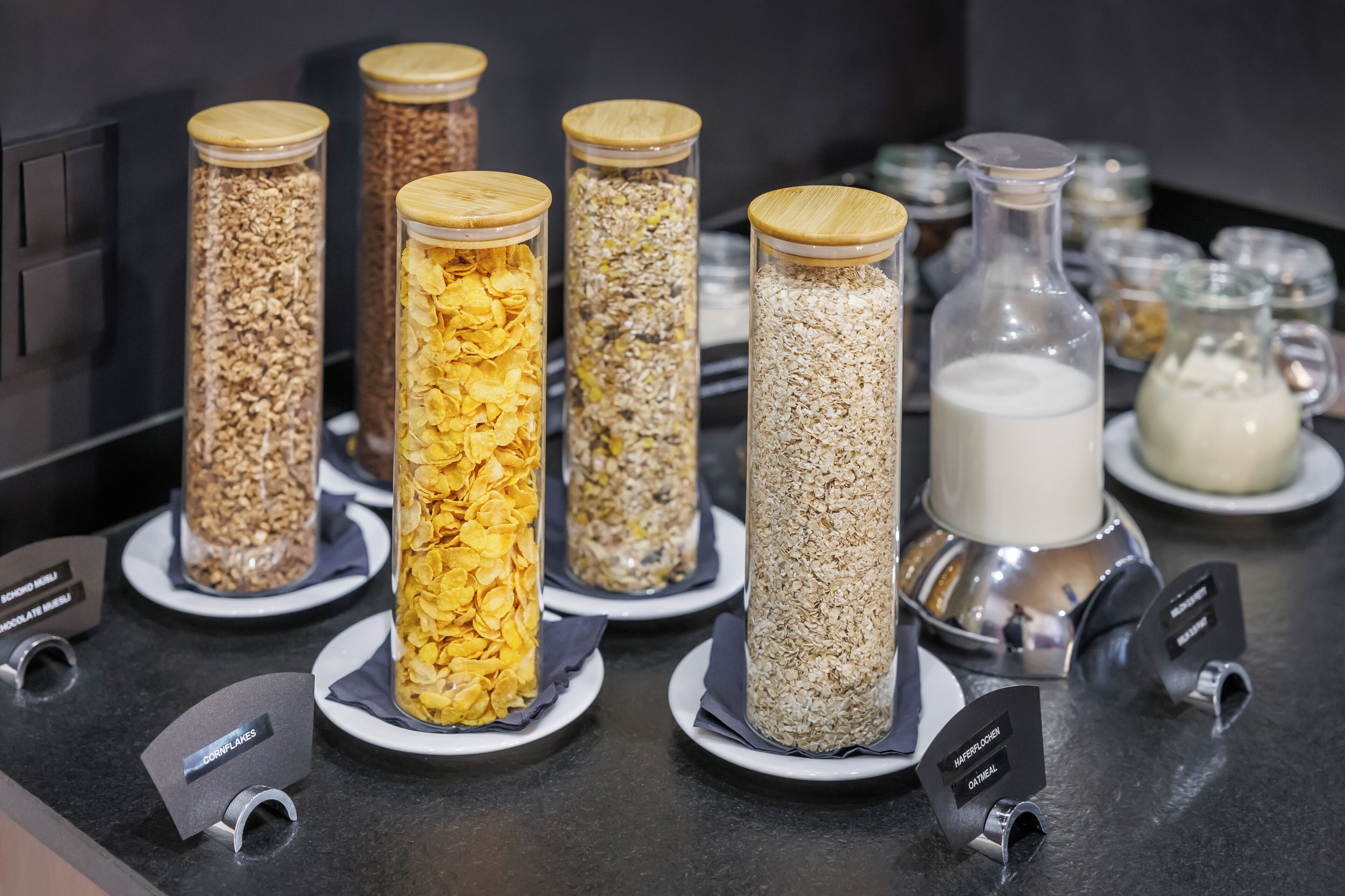 Ein Frühstücksbuffet mit verschiedenen Speisen in Glasbehältern, darunter Müsli und Milch.