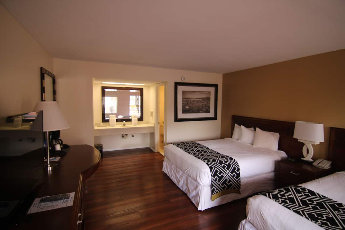 A hotel room with two beds, a desk, a chair, a lamp, a picture on the wall, and a window.