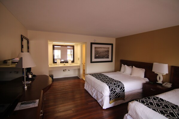 A hotel room with two beds, a desk, a chair, a lamp, a picture on the wall, and a window.