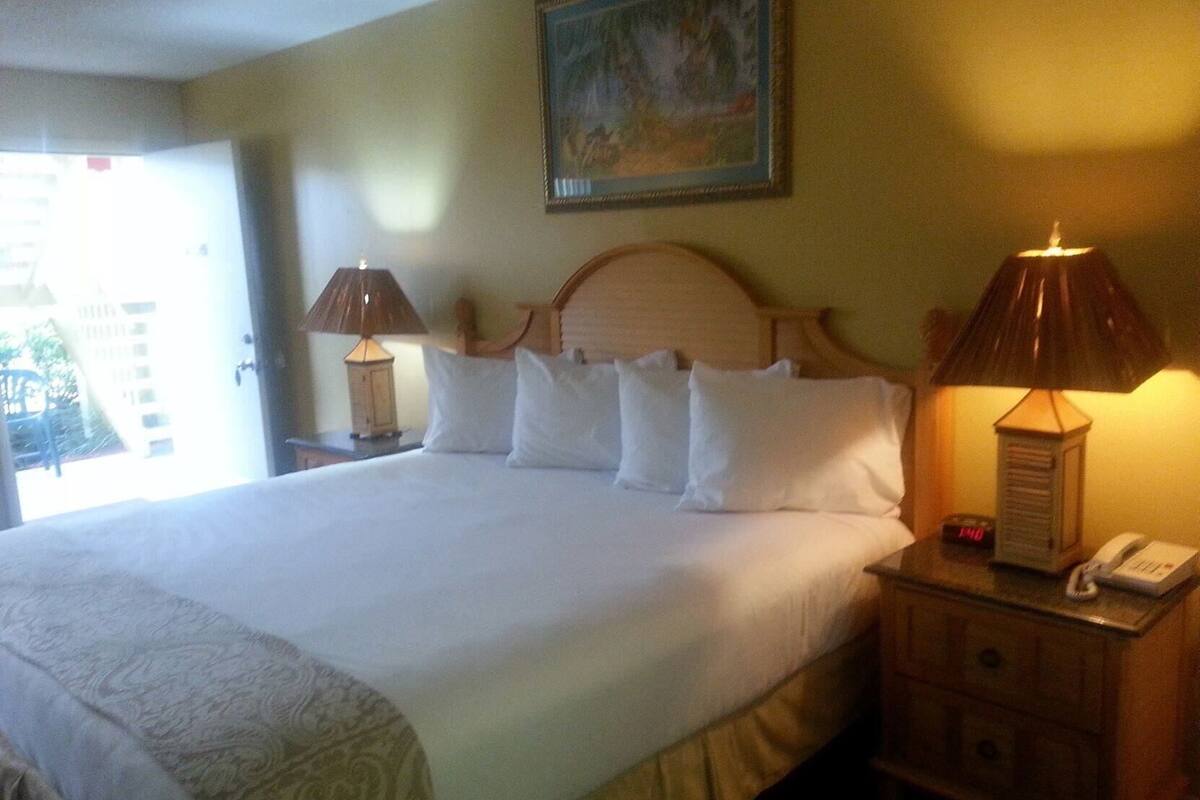 A hotel room with a large bed, two bedside lamps, a nightstand with a phone, and a painting on the wall.