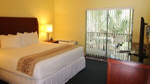 Habitación de hotel con cama, escritorio, silla, televisión y ventana con vista a palmeras.