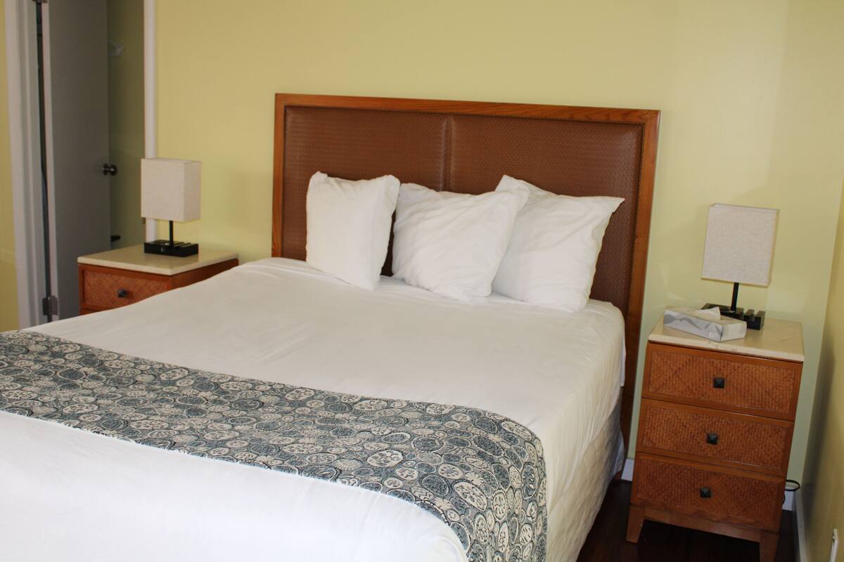 A neatly made bed with a patterned bedspread, two bedside tables with lamps, and a wooden headboard.