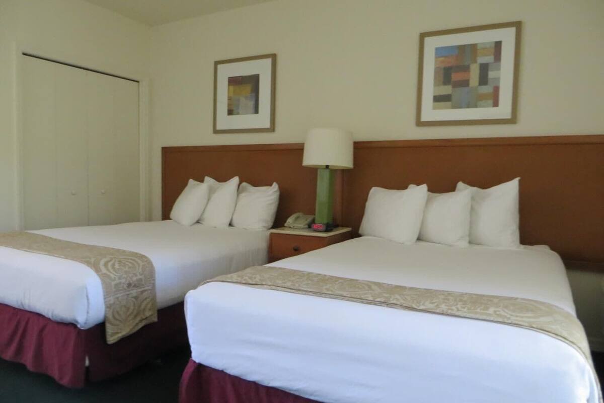 A hotel room with two beds, a nightstand with a lamp, and two framed pictures on the wall.