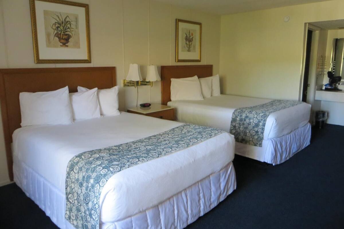 A hotel room with two beds, a nightstand with lamps, a mirror, and framed artwork on the walls.