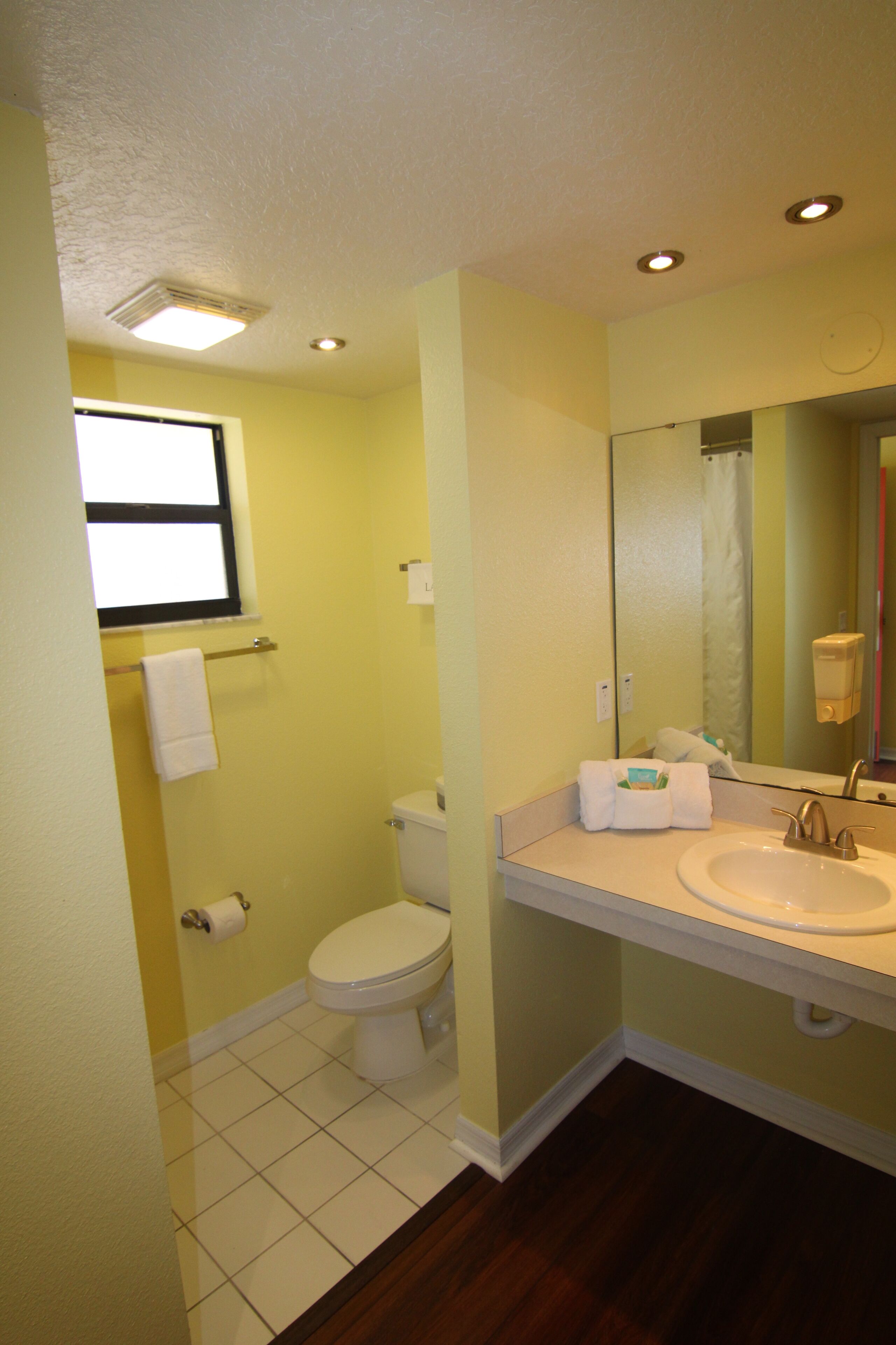 Un baño con inodoro, lavabo, espejo y una ventana sobre el inodoro.