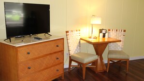 Una habitación con un aparador de madera, un televisor encima, una mesita con una lámpara y dos sillas.