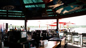 Uma área de bar com vista para a água, mesas ao ar livre e um quadro de cardápio.