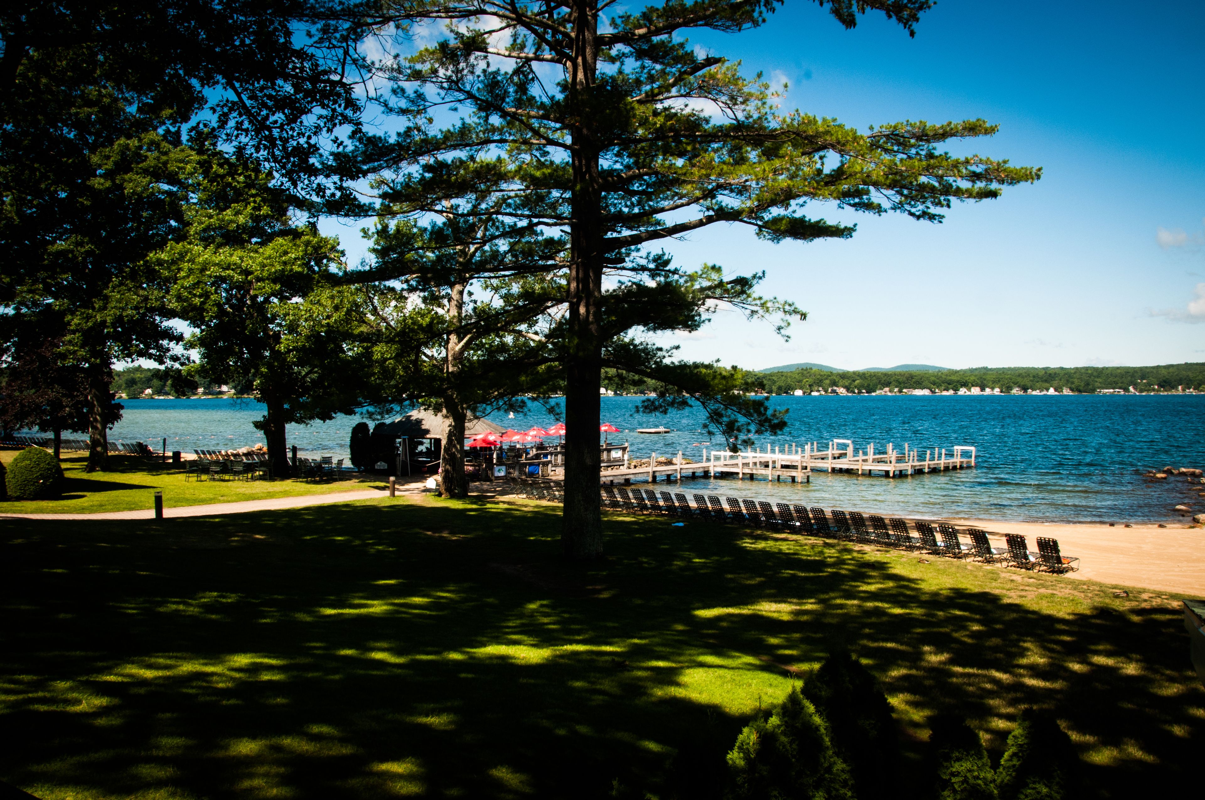 A lakeside park with a dock, chairs, and umbrellas.