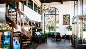 Um hall amplo com escadaria de madeira, balcão de recepção e uma grande janela em arco que oferece vista para o exterior.