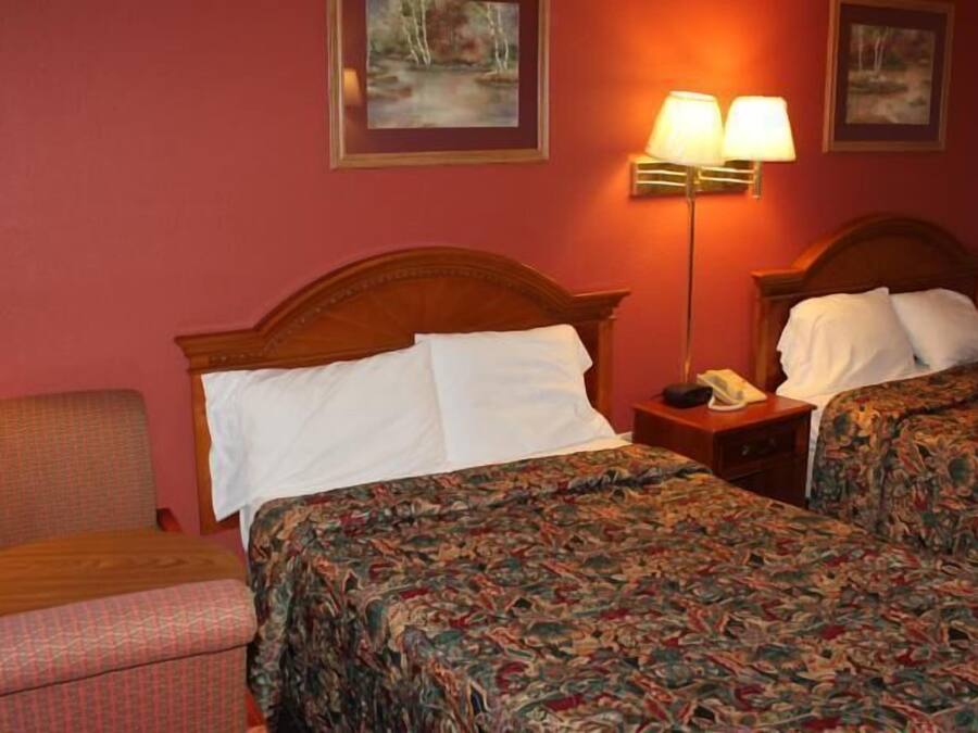 Ein Hotelzimmer mit zwei Betten, einem Sessel, einem Nachttisch mit Lampe und Bildern an den Wänden.