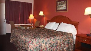 A hotel room with a large bed, two bedside lamps, a chair, a small table, and a painting on the wall. - Andrew Johnson Inn (Greeneville)