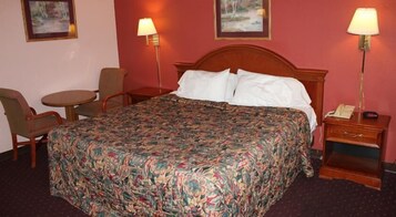 Una habitación de hotel con una cama grande, dos sillones, una mesita y dos lámparas de noche.