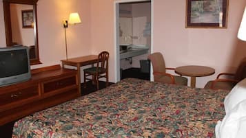 Habitación de hotel con cama, escritorio, silla, televisor, lámpara y una mesita.