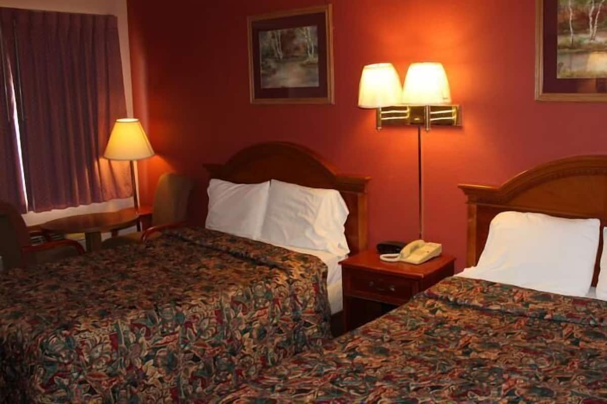 Quarto de hotel com duas camas, uma mesa de cabeceira com abajur e um quadro na parede.