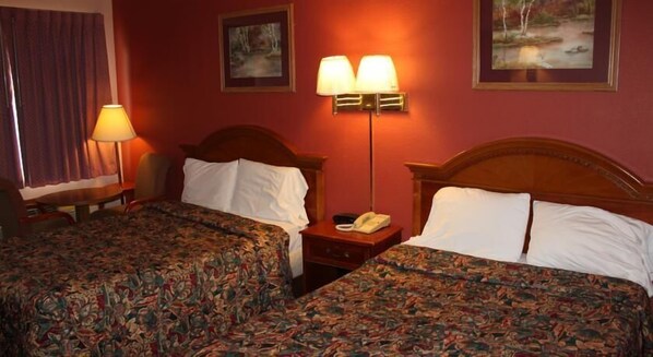 Una habitación de hotel con dos camas, una mesita de noche con lámpara y un cuadro en la pared.